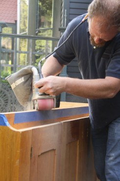 Once everything is marked, Donbeck removes material from the base, using a belt sander. Here, to ensure a crisp line at the floor and wall, he maneuvers the sander so he bevels slightly away from the front plane.