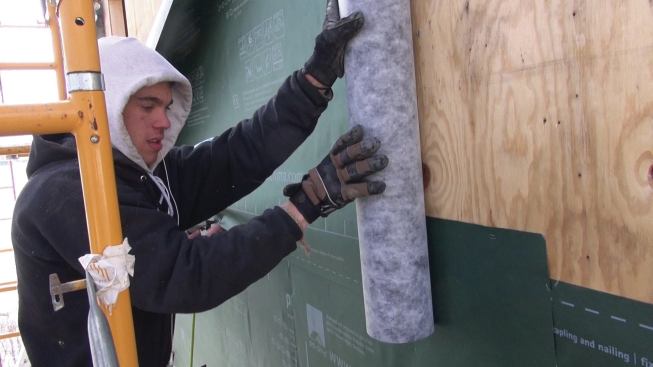 The crew pulls the Pro Clima DA membrane tight over the existing sheathing.