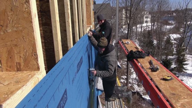 After rolling out Pro Clima Solitex Mento membrane directly over the I-joists, the crew stretches the fabric tight.