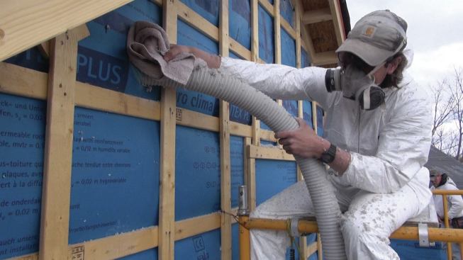 The strapping secures the fabric to the wall, enabling the crew to blow the I-joist cavities with dense-blown cellulose insulation.