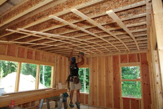 After snapping all of our lines, we lean lengths of strapping against the top plate at one end of the room. One carpenter then picks up a piece, places it on the line, and tacks it to a joist roughly in the middle of the length of strapping.