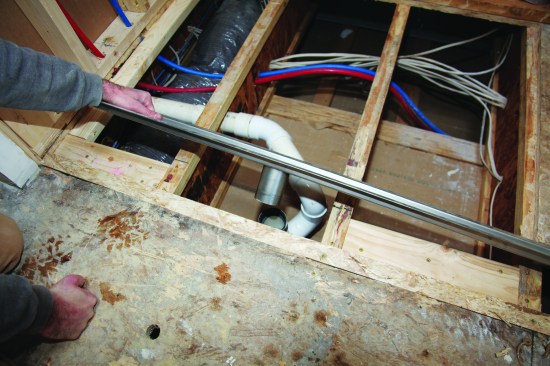 To rough-in the smaller shower, the crew installed 2-by vertical blocking to the web of the outer-bay joists to support horizontal blocks between the joist flanges. The center bay was left open for the drain stub. 