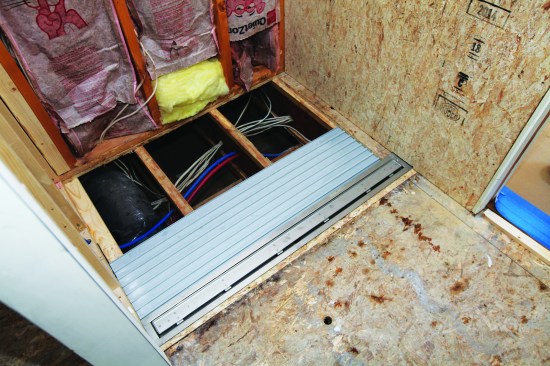 The crew cut the panels to length, trimmed the last panel to width, then slid the assembled pan base under the drain flange and fastened it to the joists. 