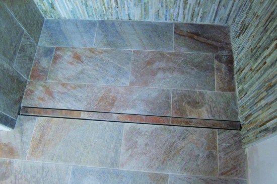 The drain cover is a stainless steel tray with fixed metal feet that stand in the drain channel. Raised edges on the tray contain the tile, which gets installed in thinset and grouted.