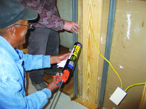 After slipping the floor-plate brackets onto the bottoms of the split studs, I held the assembly in place while my helper ran a bead of construction adhesive on the drywall behind each stud position.