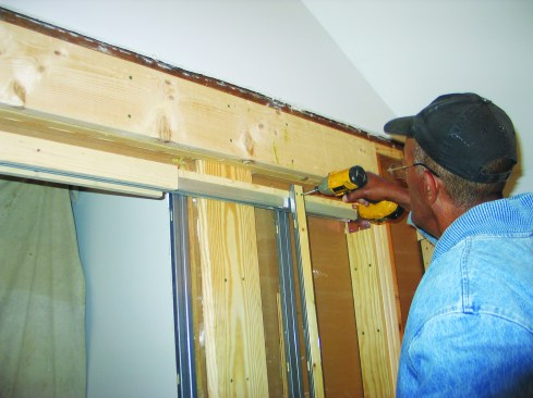 To install the other halves of the two split studs that faced the bathroom side of the pocket, we slipped the studs into the floor brackets, positioned them against the header, and drove two screws through each stud to anchor them in place.