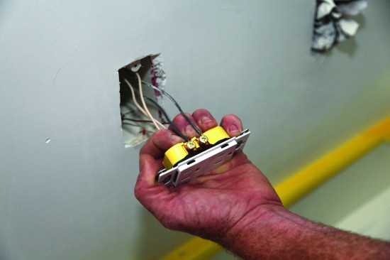 After flipping the receptacle over to the opposite side, he slips the hot (black) conductors over the brass screws and snugs them down tight.