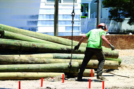 A crew member fastens a loop of chain around each piling, and the crane lifts the piling and swings it to the hole.