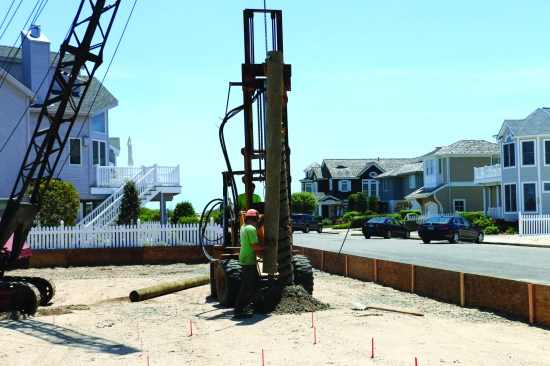 The crew member then guides the piling into the hole and levels the ground around the piling with a shovel.