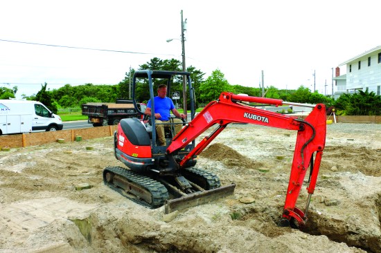 A mini-excavator roughs out the trenches, digging between the pilings.