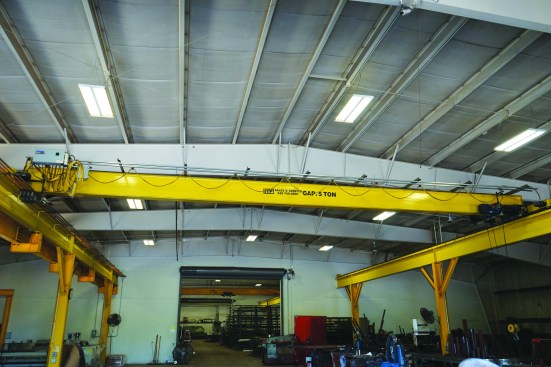 Overhead cranes help move heavy beams safely around a shop.