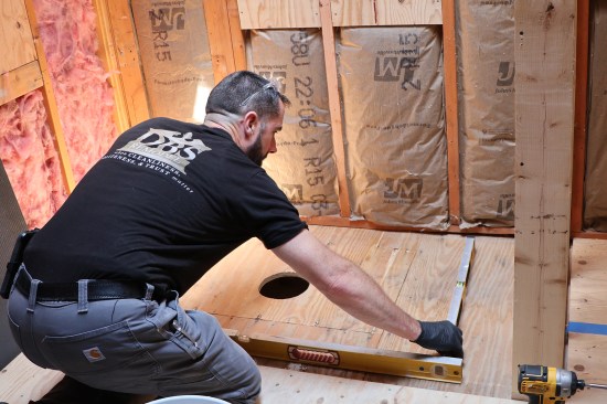 The subfloor is checked for level prior to installing a pre-pitched shower pan. The author can apply slightly thicker amounts of thinset to lower areas to micro-adjust the shower pan for level.