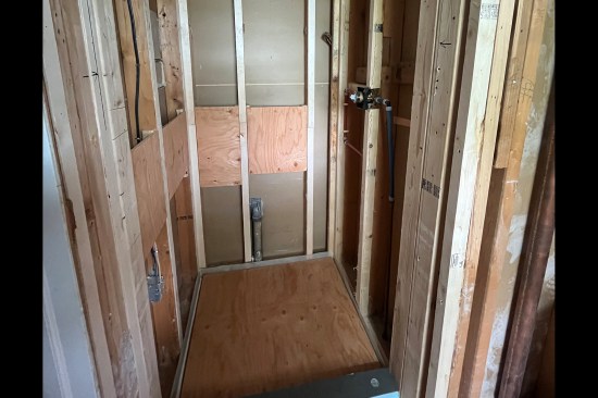 The studs in an existing shower shimmed to plane out wall. Plywood blocking installed for future grab bars (the author takes photo to mark the blocking locations prior to installing tile backerboard).