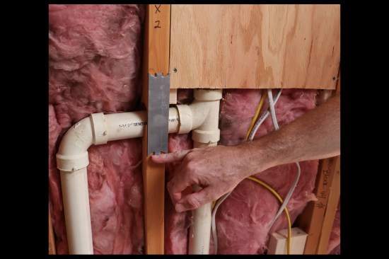 Here, a metal protection plating is tacked into place by the plumbing sub. The author removes the protection plates, chisels out the 2-by material, then reinstalls them flush with the wall studs to prevent bulging of the backerboards.
