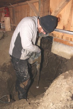 Chris drills holes for steel reinforcement in the precast footing pad using a hammer drill.