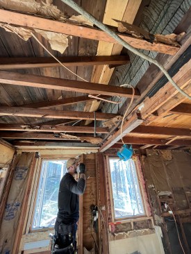 The owner wanted to raise the roof where the old porch roof had been to create a partially cathedralized area. Here the author is preparing to remove the porch ceiling and prepare to install a new beam to support the combine roof/wall/floor structure.