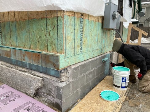 With the framing buttoned up, a member of the O-A Design-Build crew coats the sheathing and foundation with GCP's Perm-A-Barrier primer. The primer can be applied at temperatures down to 25 degrees F. and is designed  to create a tenacious bond to the substrate - a good practice when applying peel-and-stick flashing in colder weather.