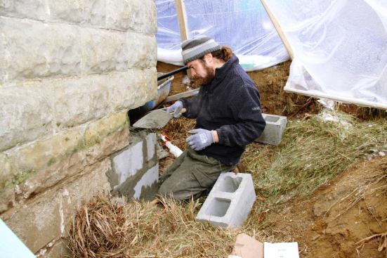 Portland mason Joe Martignetti repairs the building’s block foundation last winter. The existing foundation wall remained porous to air and moisture after the patching and repointing, but the crew applied rigid foil-faced polyiso to the interior to control heat, air, and moisture flow.