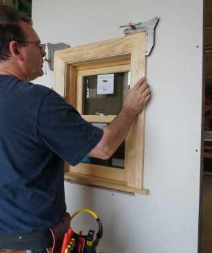The casing assembly sits on top of the stool horns while the author aligns it with the reveal marks on the extension jambs.
