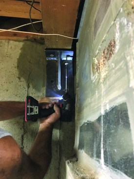 Because the bracket would be bolted into the existing concrete, the author was able to install it before the parging had cured completely. He began by driving structural screws through predrilled holes in the bracket and up into the girder.