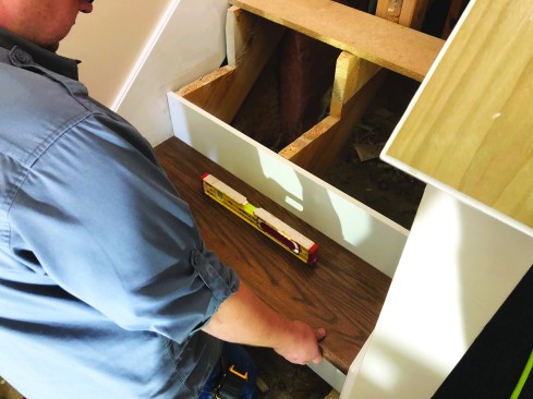 He dryfits the tread and does an initial check for level. If the gap between the stringer and tread is 3/8 inch or more, he glues in thin plywood layers to build the stringer up to a rough height for shims.