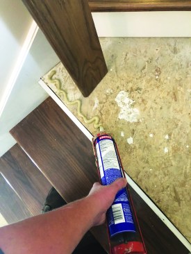 After the new treads and risers are installed, the author applies adhesive for the nosing on the stair landing.