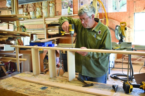 After predrilling for the screws, the author attaches one rail to the treads and the top rung.