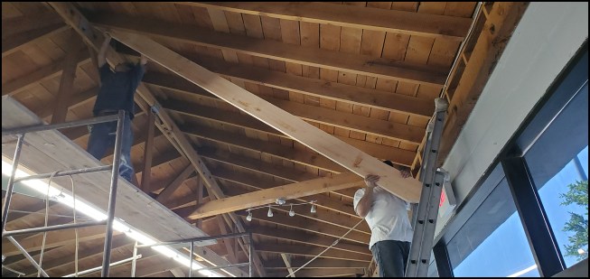 Roof connections. Crew members sister new 2x8s onto existing rafters at steel angle diagonal brace locations above the storefront entry.