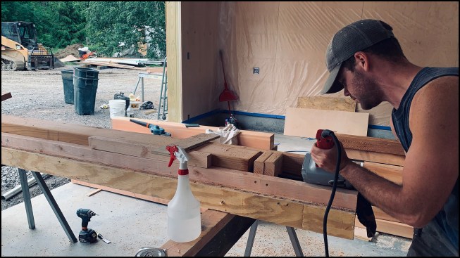 Crew member Nathan Tuttle bores into a 6x6 cedar post with a 2 1/4-inch-diameter Forstner bit attached to an extension rod and a corded drill.