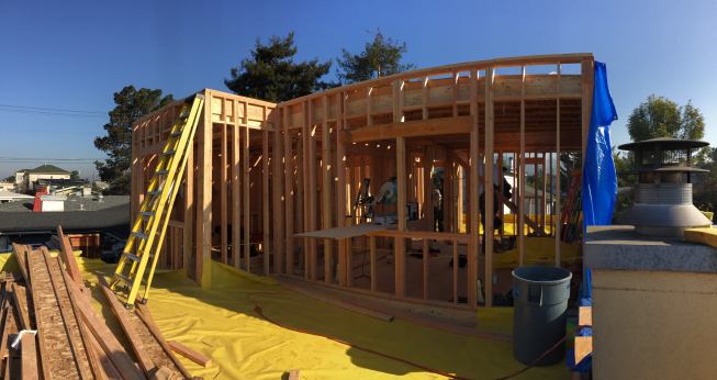 A view of the newly framed second story walls, after the temporary tarp roof was removed. The yellow poly in the foreground shows where a walkable outdoor deck will be, accessible from the second floor living space, overlooking the back yard.