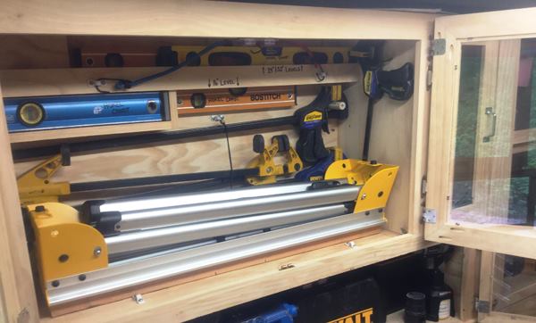 The next cabinet in has two saw horses, some smaller levels and 4-foot clamps. From the inside of the door you can see that the joints are mitered and held together with pocket screws. The acrylic panels are held in place with the kind of glazing points used to hold glass in old-fashioned—glazed windows. Note the white clips at the bottom front and back upper wall, which are used to tie/secure tools in place.