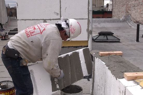The underside of a piece of 4-inch EPS foam is buttered with cementitious mortar …