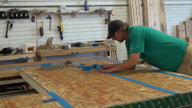 Steve Greenleaf applies ProClima Vana tape to the nailing lines and seams of the OSB wall sheathing for the inner 2x4 wall of the panel. This tape will seal against any leaks through nail penetrations in the OSB. It also serves to air-seal the screw penetrations created when wood I-joists are attached over the sheathing during the next step in the panel construction process.