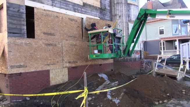 With one carpenter cutting OSB sheets on the ground and two working from the bucket of a lift, the crew works its way up the side of the building.