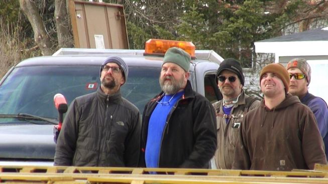 The team watches as the crane maneuvers the heavy modular unit toward the foundation, working around streetlights, wires, and trees.