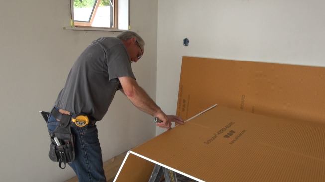 Boucher cuts Kerdi-Board tile underlayment with a razor knife. The foam board is much easier to cut than traditional cement board, and pre-preinted lines at one-centimeter spacing make it simple to mark cut lines.