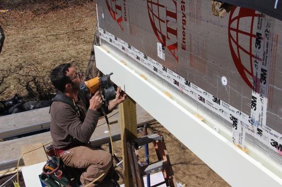 Pollard nails fascia to ¾-inch strapping applied over the foil-faced rigid insulation. Trim elements are spaced off the foil faced polyiso foam to facilitate the drainage of wind driven water and drying of the wood trim. The beam trim shown here is unusual, Pollard points out: it is the only trim or siding element on the building exterior where the space behind the trim has no air inlet at the bottom or exhaust at the top for air to flow freely. However, the air space behind the wood trim, combined with a coat of primer and first coat of paint, should still add to service life of the wood and the paint job.