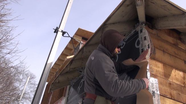 Carpenter Shane Fenton applies 3M 8067 flashing tape to the Grace membrane on a wall and wraps the tape around the corner to complete the seal. The 3M tape stays flexible and sticky at surprisingly cold temperatures, but the crew needs to work without gloves when applying tape, in spite of the bitter cold weather.