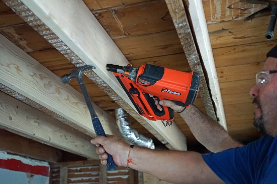 A screw in the edge of the sister joist and a hammer help pull the sisters flush to the bottom edge of the existing joists.