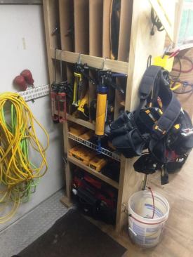 Shot near the front right side of the trailer, the vertical slots in this unit hold cordless tools (lower) and pneumatic nailers (upper). The cords to the left are hanging from the back of the side door of the trailer. Note the old fashioned window lift hardware and bungee used to keep the drywall bucket from sliding around.