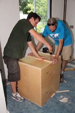 Inside the kitchen, Joe and Jeff fasten cleats to the upper cabinet.