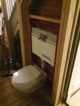 Even with the framing on the flat, extra space was needed for code-required clearance for the wall-hung toilet. The framing was recessed as far as possible below the stairway. Here the tank is installed and the toilet hung in place temporarily.