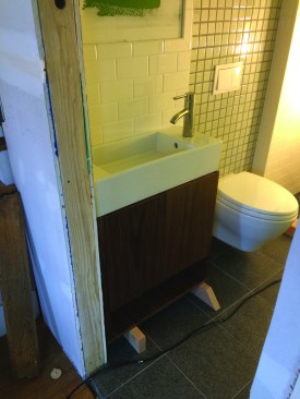 In keeping with the wall-hung toilet, the vanity—made from a kitchen wall cabinet—was mounted on the wall. Here the bathroom is tiled and vanity rests on blocks before being secured in place.