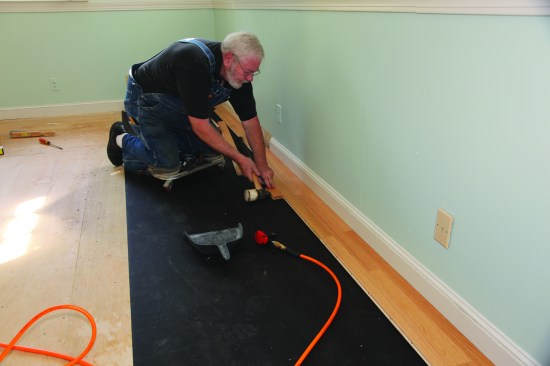 To protect the finished surface of the flooring, author uses a scrap block to tap a strip snugly against the neighboring board.