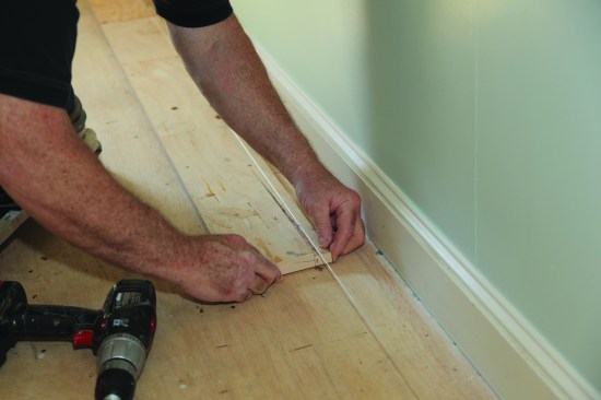 A straightedge screwed to the floor will keep the starter course straight as it's being scribed to the wall. A notched stick helps place the straightedge precisely parallel to the string.