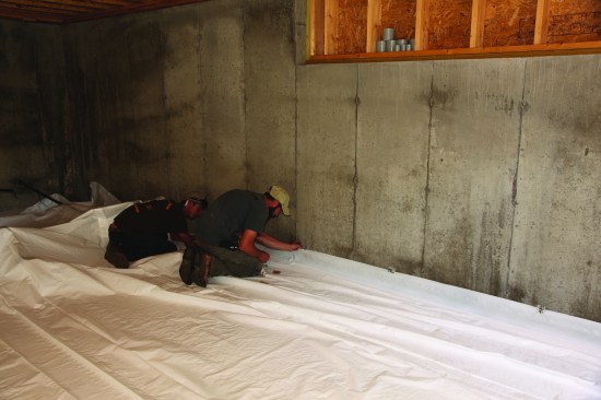 After snapping a line on the foundation wall, the crew tacked the poly to the wall with small pieces of tape.