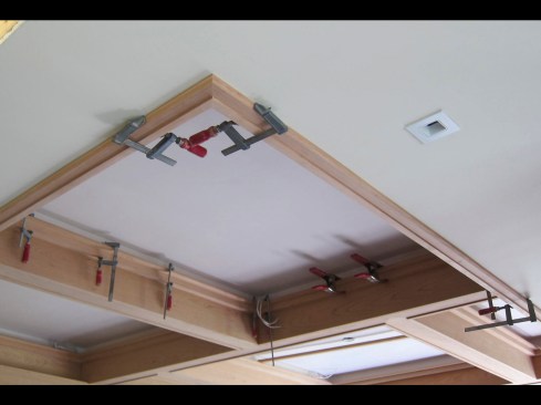 With the bottom edge falling an inch below the ceiling drywall, a narrow picture-frame trim was run around the fascia and joined with Domino inserts at the mitered corners. The picture frame was glued, clamped, and finish-nailed to the fascia in place.
