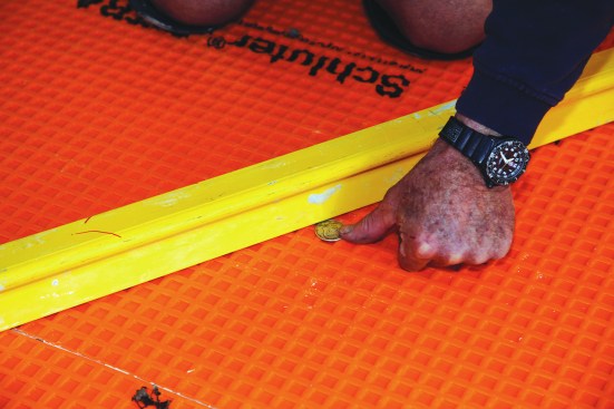Installing large-format tile requires a subfloor that is almost perfectly flat. The author checks the floor by trying to insert a silver dollar (or other 1/8-inch-thick spacer) under an 8-foot straightedge.