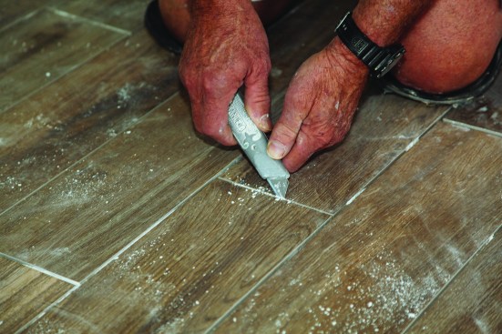 Before grouting the floor, the author cleaned and prepped the tile. He used a utility knife to scrape out the excess dried thinset from the grout joints.