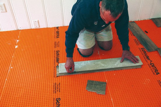 Starting the first course with a quarter-size tile in the corner, the author put a full tile over the most trafficked area of the threshold, which helped to minimize the chance for cracking. Avoiding a grout line in the doorway also looked much better. The author marked the end scribe on the full tile and then flipped the tile over to mark the strip he needed to remove along one edge.